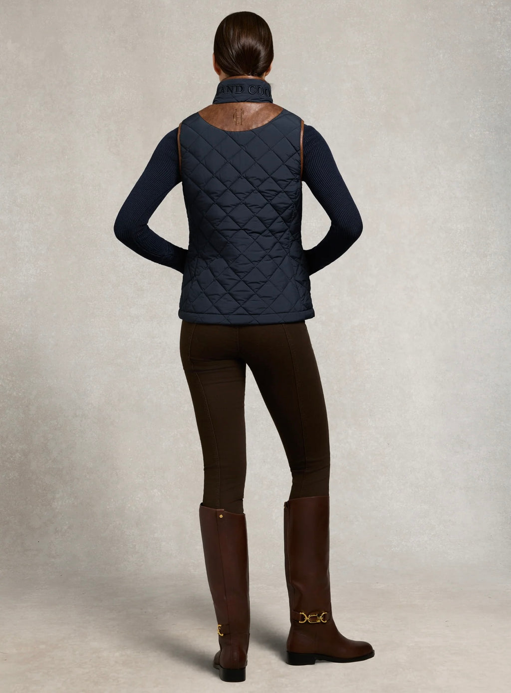 Person wearing a navy quilted jacket, black leggings, and brown boots on a neutral background