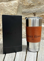 Stainless steel tumbler with brown leather wrap and black sleeve on wooden surface