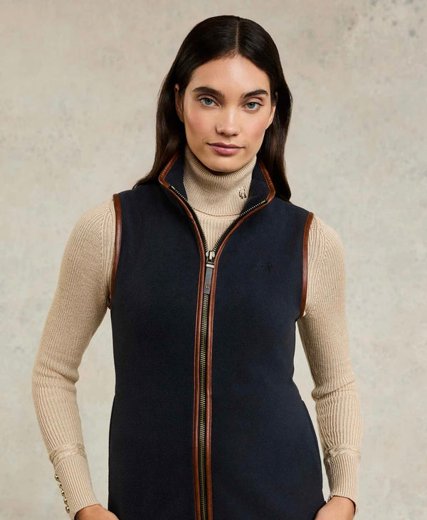 Woman wearing a navy vest with brown accents on a neutral background