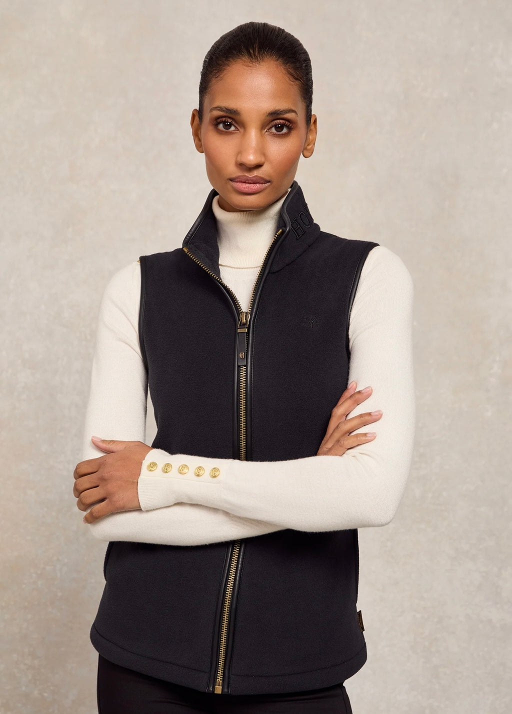 Woman wearing a black vest over a white sweater against a neutral background