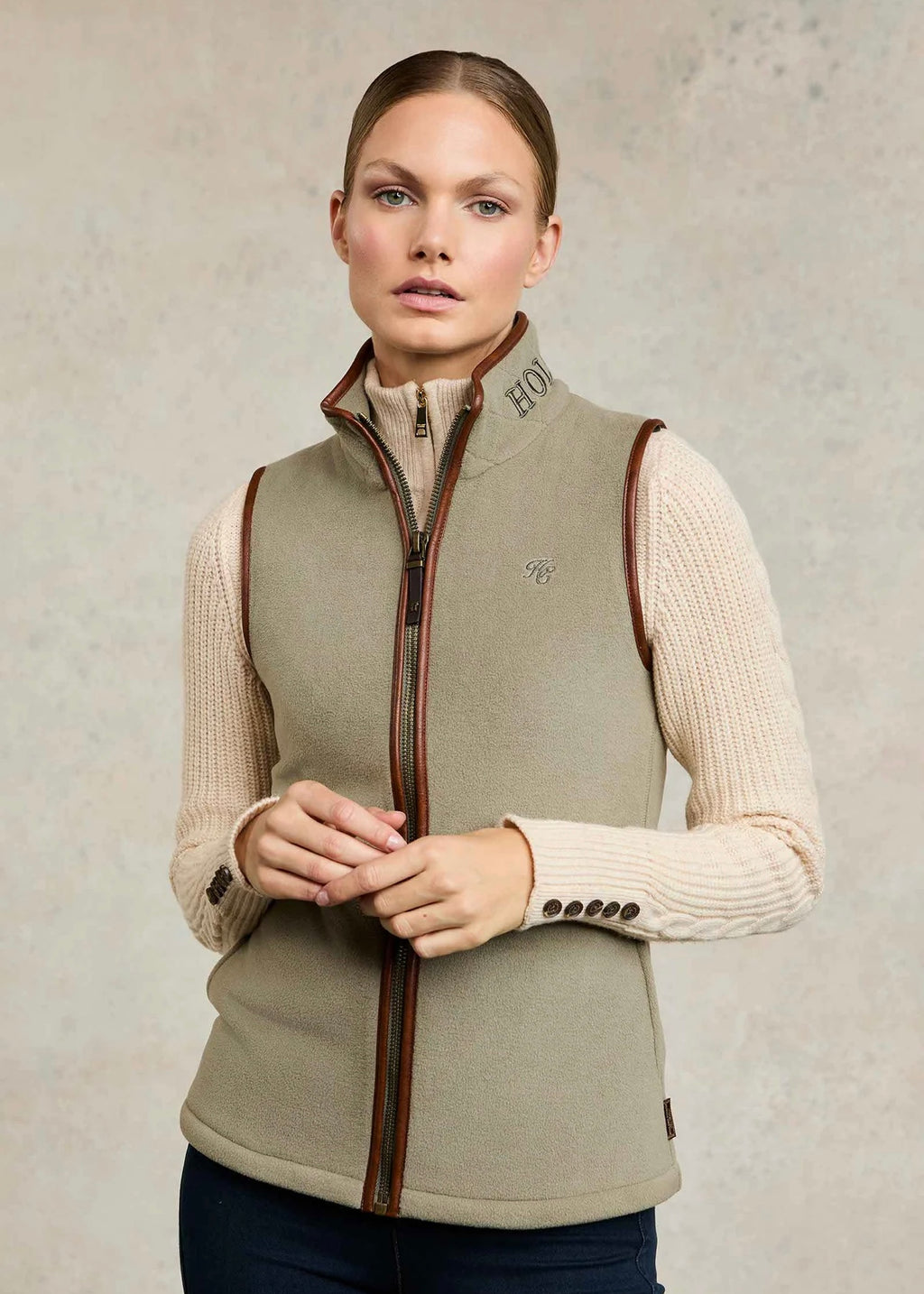 Woman wearing a beige vest over a cream sweater on a neutral background