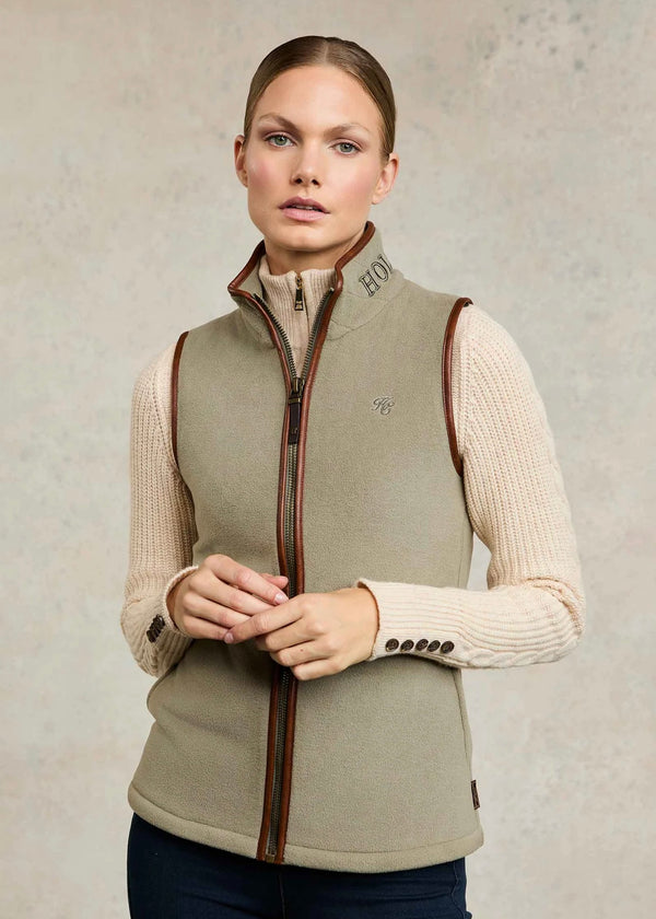 Woman wearing a beige vest over a cream sweater on a neutral background