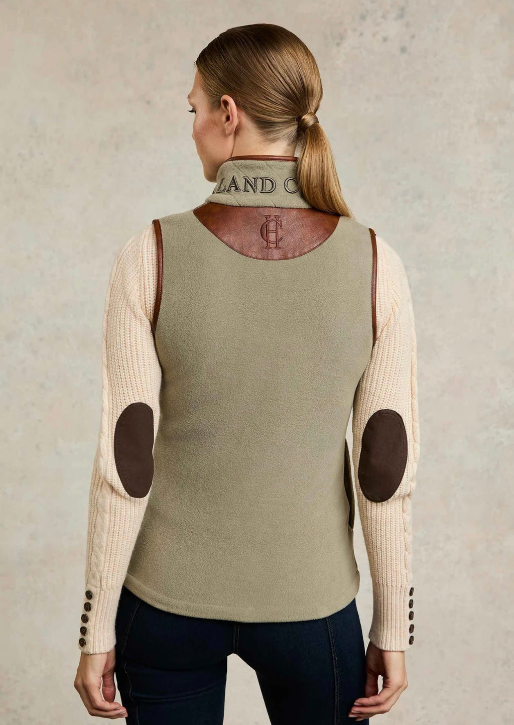 Person wearing a beige sleeveless top with brown elbow patches on a neutral background