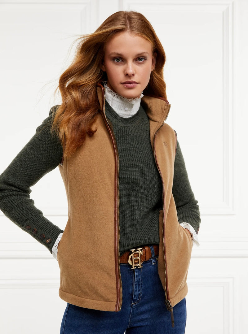 Woman wearing a brown vest over a green sweater with a white shirt underneath, on a white background.