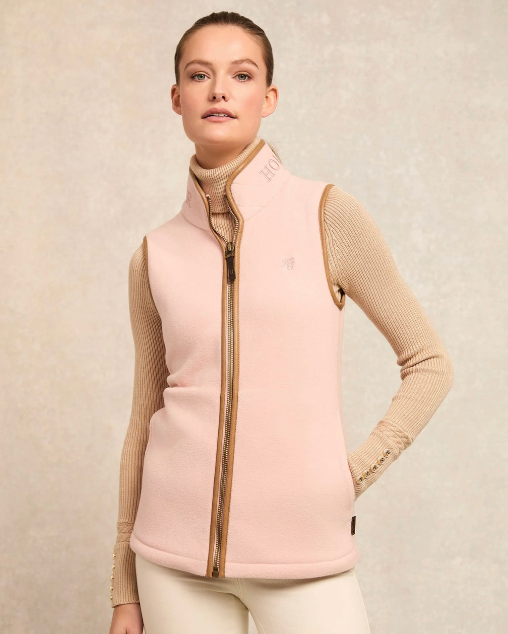 Woman wearing a light pink vest over a beige sweater on a beige background