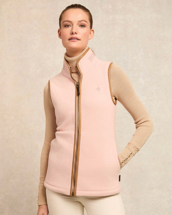 Woman wearing a light pink vest over a beige sweater on a beige background