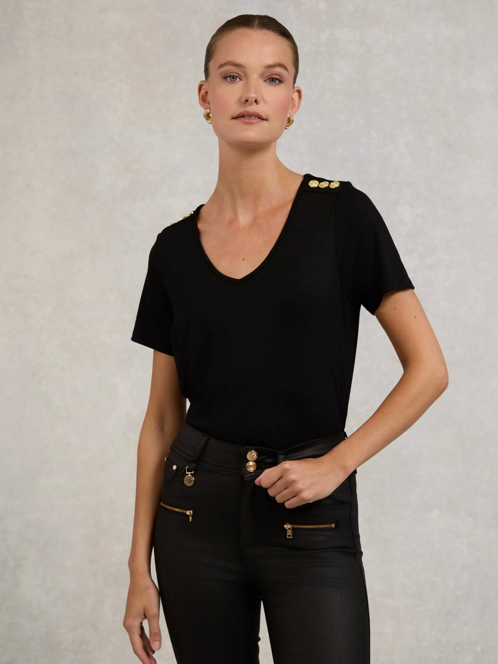 Woman wearing a black outfit with gold buttons on a neutral background