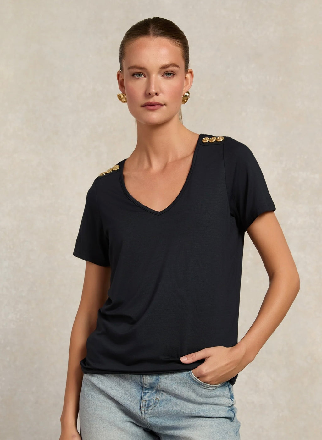 Woman wearing a black t-shirt with gold buttons on a beige background