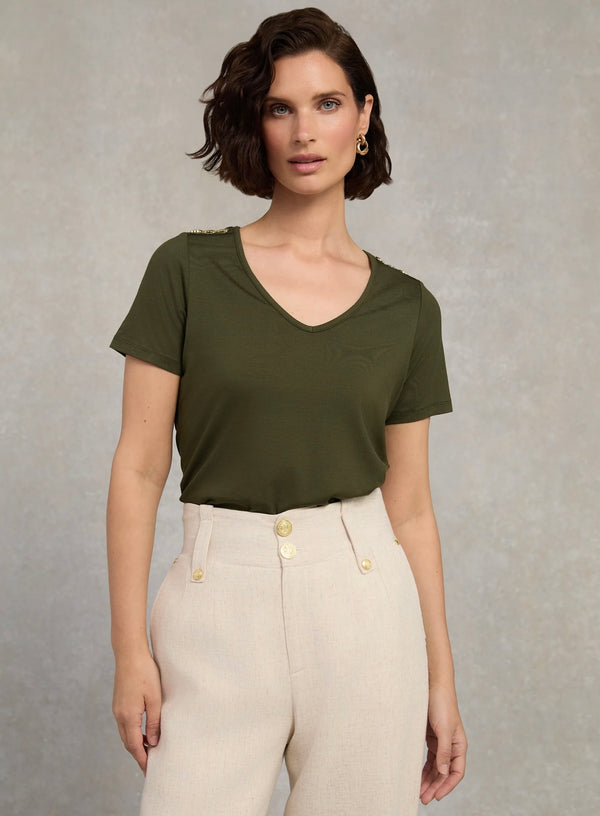 Woman wearing an olive green top and beige pants against a neutral background