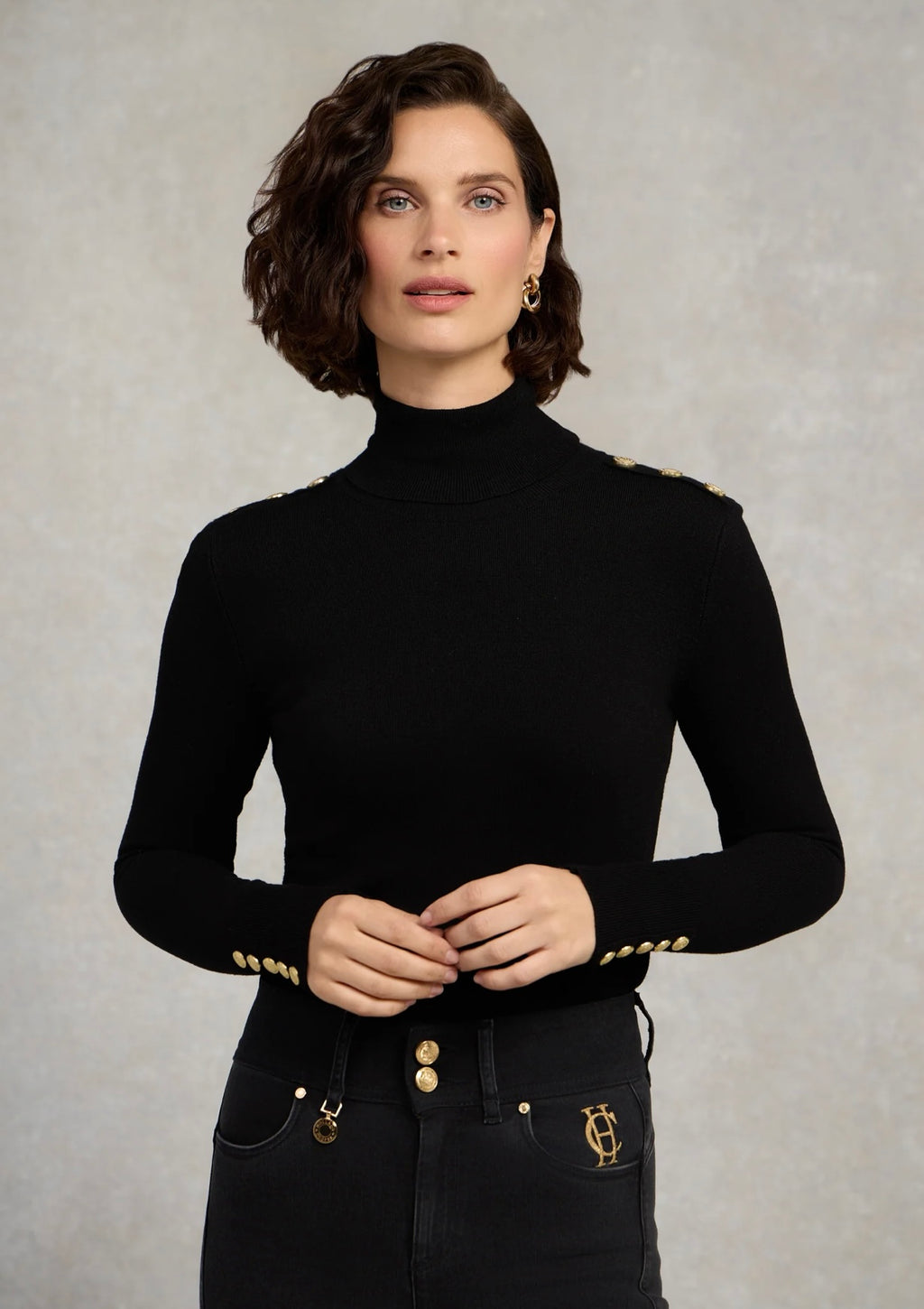 Woman wearing a black turtleneck with gold accents against a neutral background