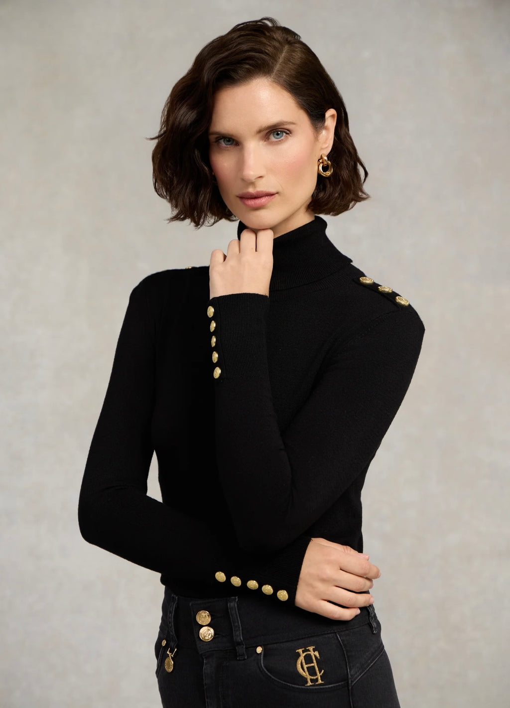 Woman wearing a black turtleneck sweater with gold buttons against a neutral background