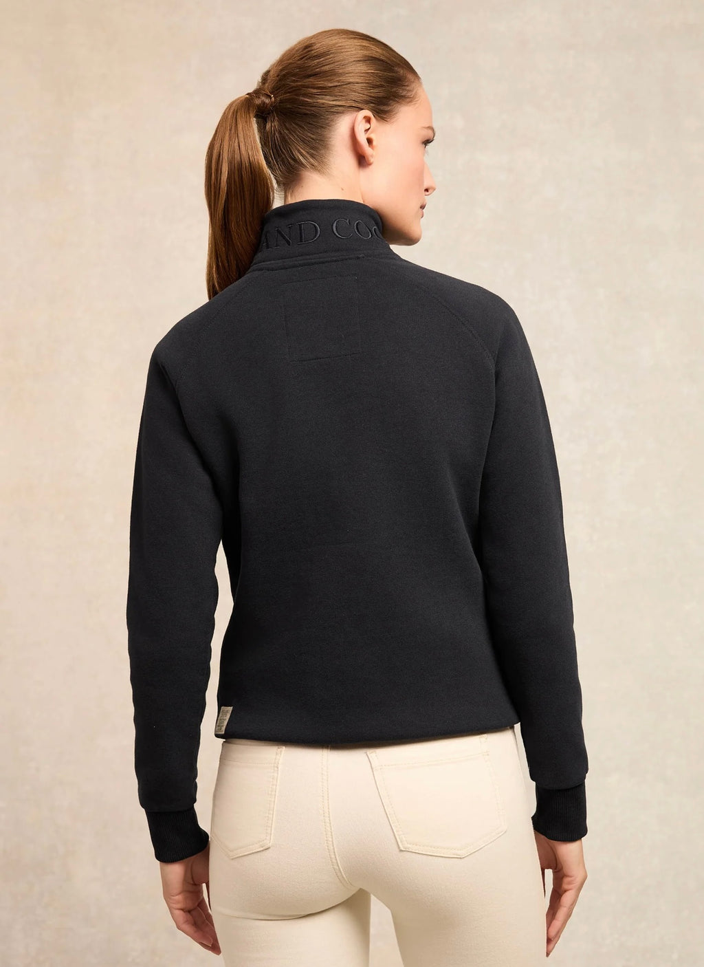 Person wearing a black equestrian jacket with a visible brand logo on a beige background