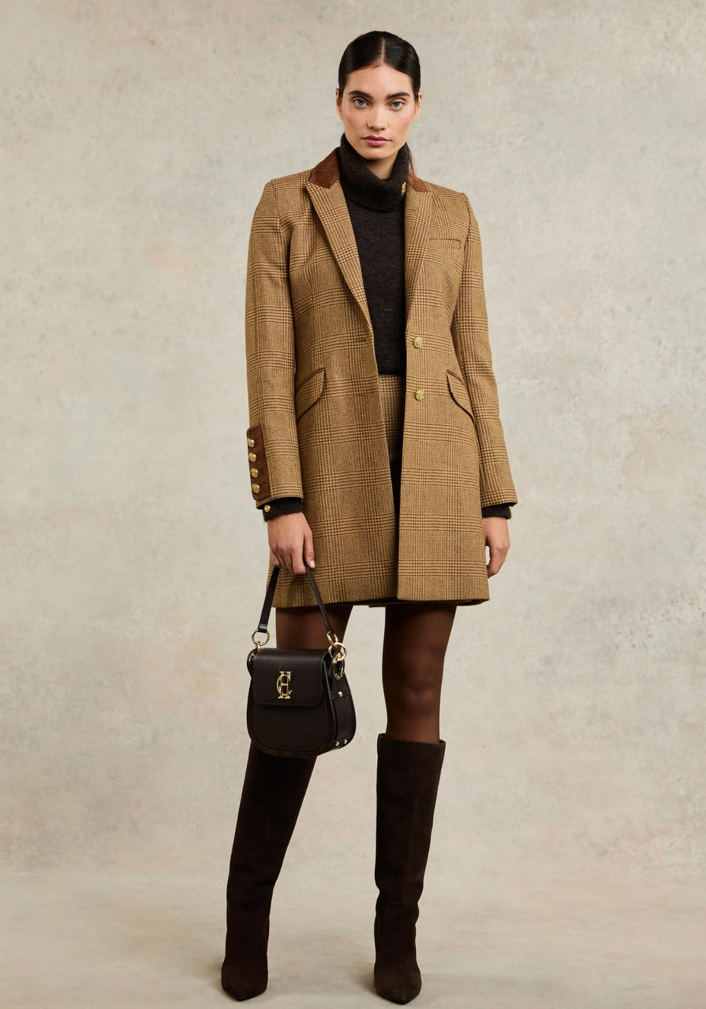 Woman wearing a brown checkered coat with a black handbag and knee-high boots on a beige background