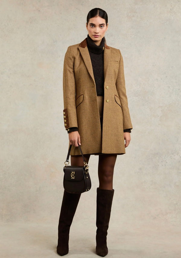 Woman wearing a brown checkered coat with a black handbag and knee-high boots on a beige background