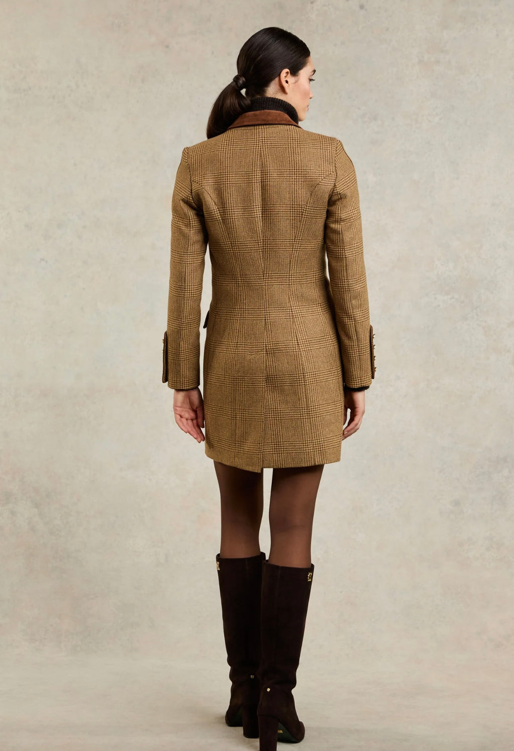 Woman wearing a brown checkered coat and black boots on a beige background