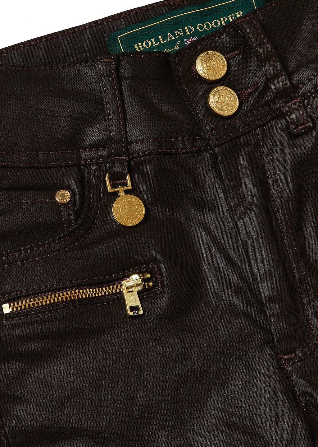 Close-up of black pants with gold buttons and zipper, featuring Holland Cooper branding.