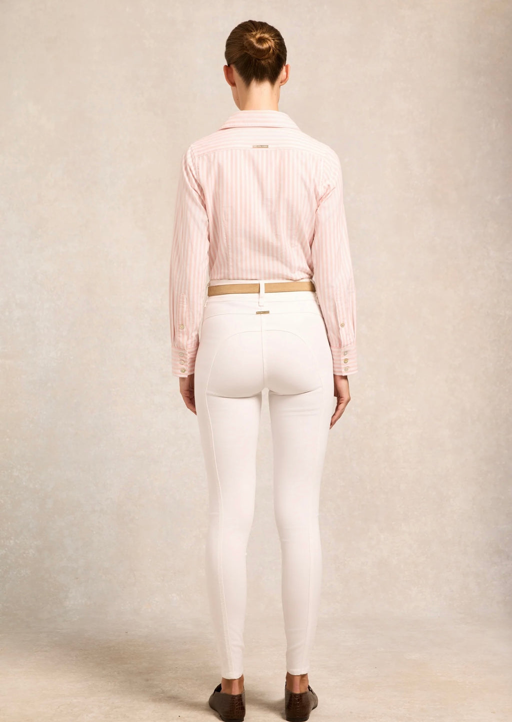 Person wearing a pink striped shirt and white pants on a plain background