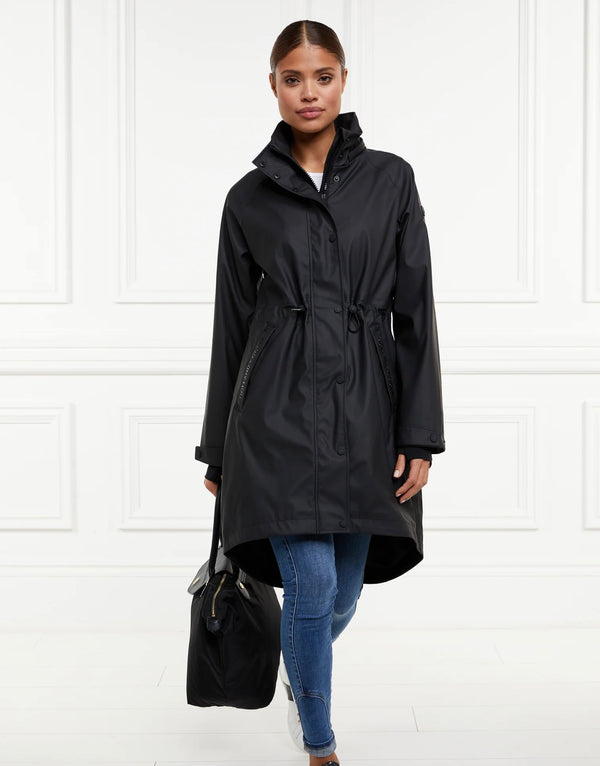 Woman wearing a black raincoat holding a black bag against a white background