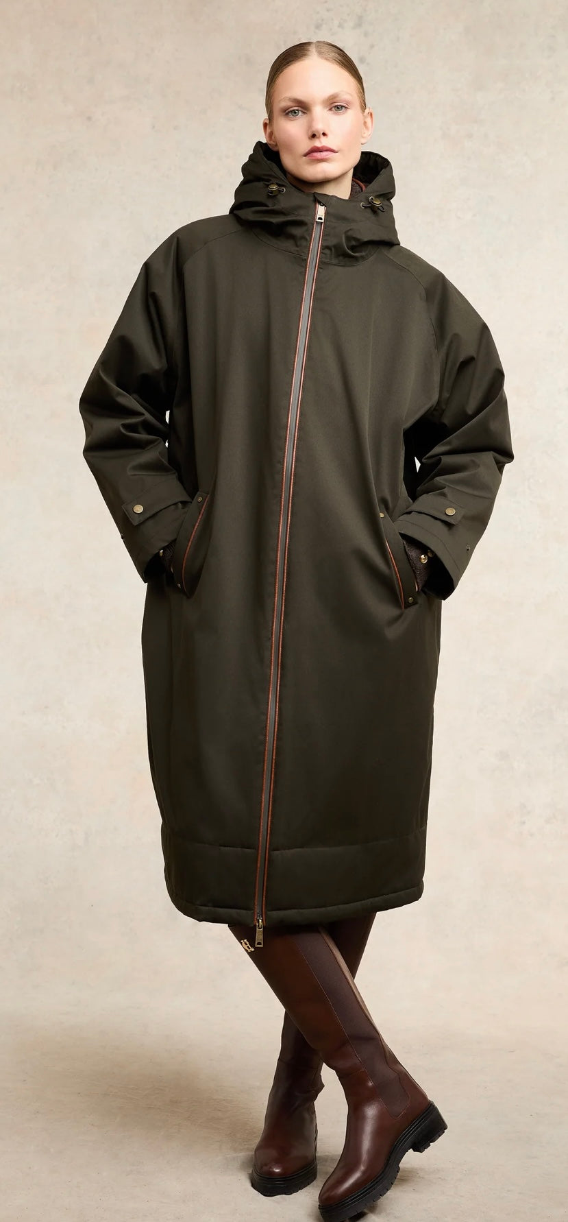 Woman wearing a long dark coat with a high collar on a neutral background