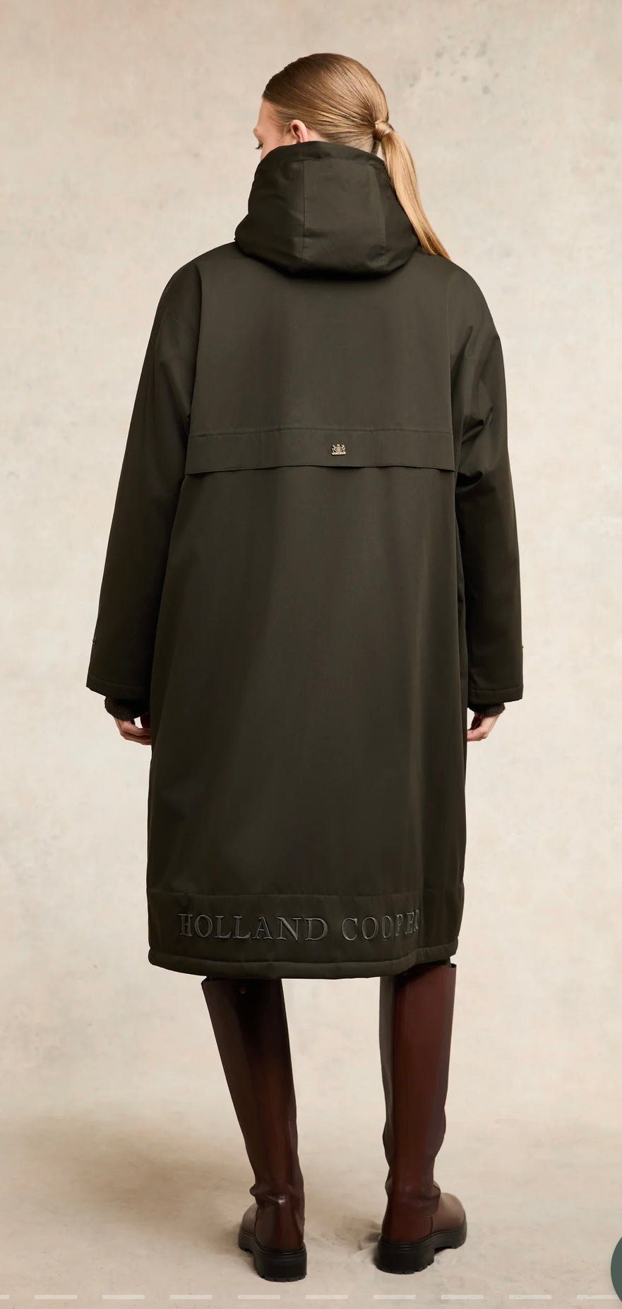 Person wearing a black coat with 'Holland Cooper' branding on a beige background