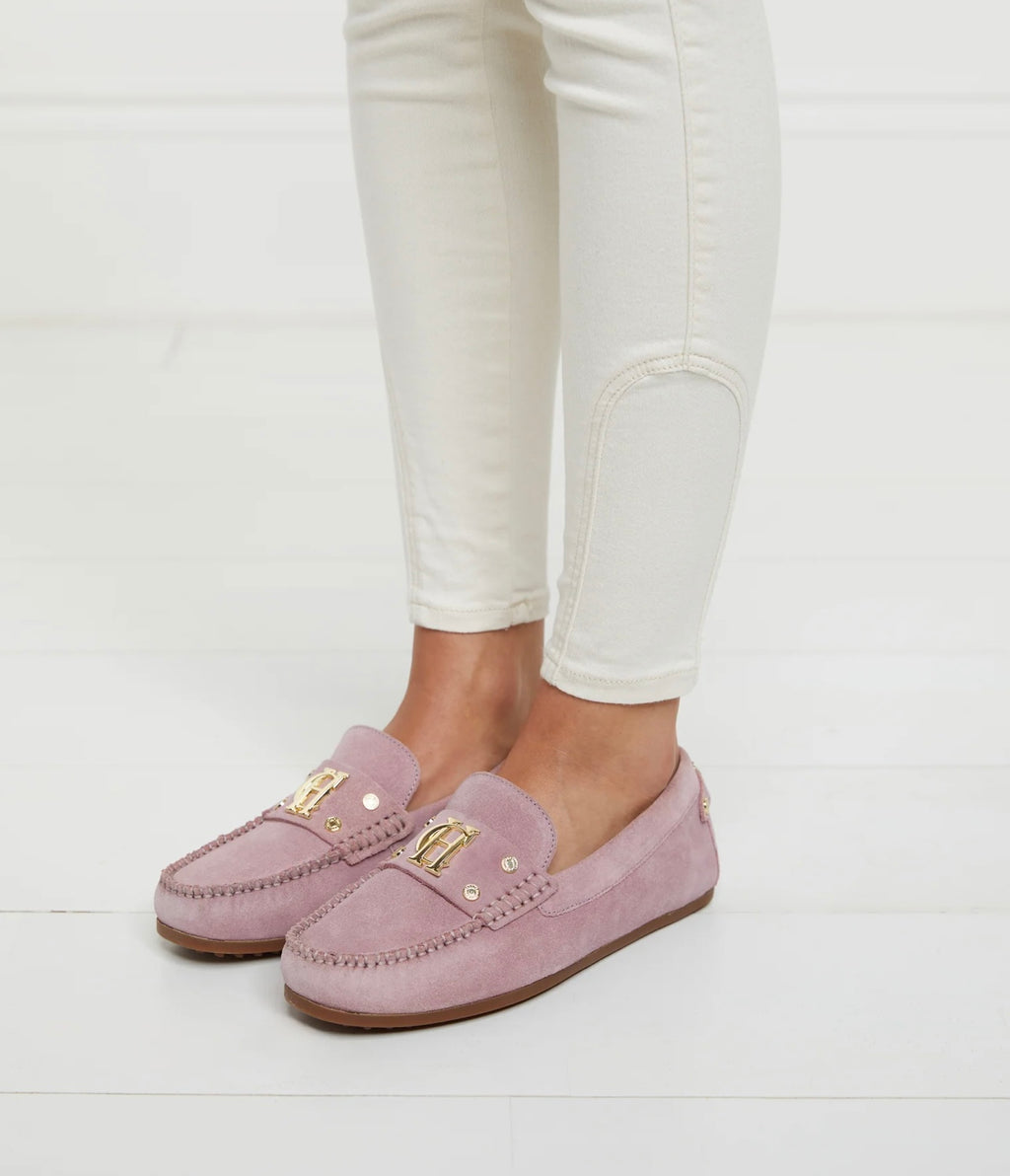 Pink loafers worn with white pants on a light gray background
