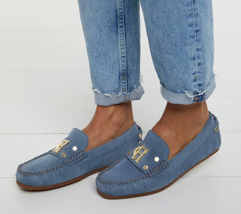 Blue loafers with gold accents worn with rolled-up jeans on a white background