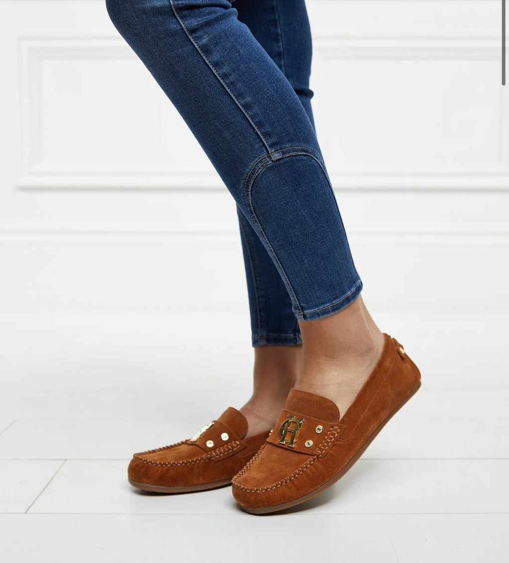 Brown loafers worn with blue jeans on a white background