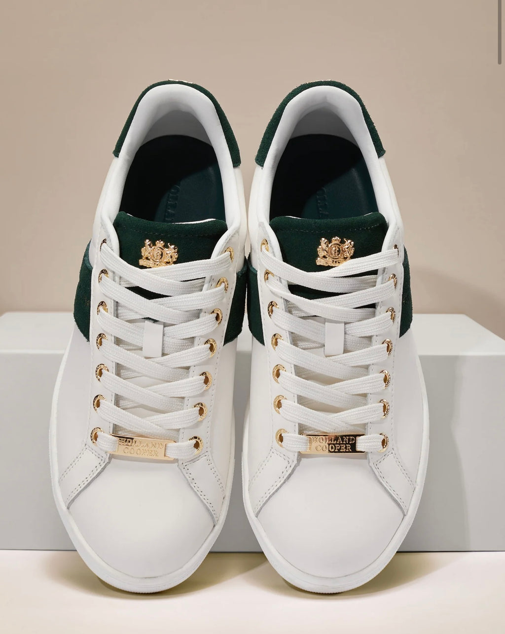 White sneakers with gold accents on a white platform against a beige background