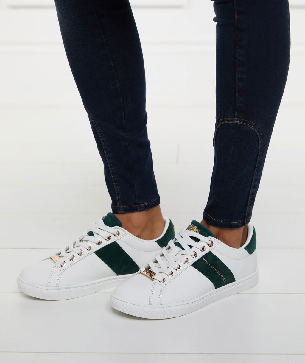 White sneakers with green accents worn with dark jeans on a white background
