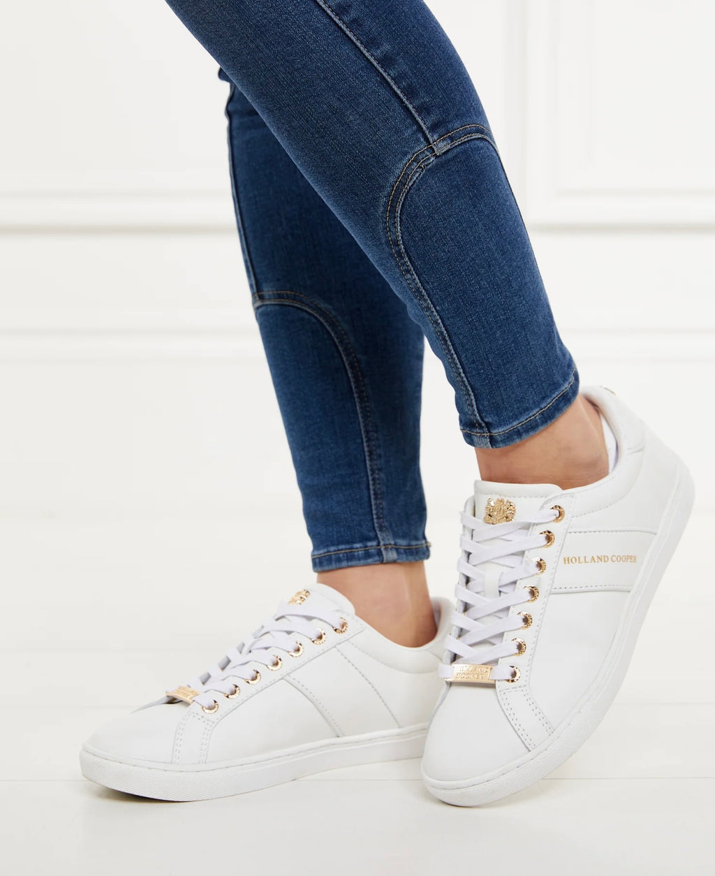 White sneakers with gold accents worn with blue jeans on a white background