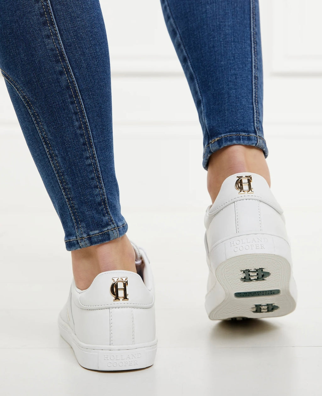 White sneakers with a logo worn with blue jeans on a light background