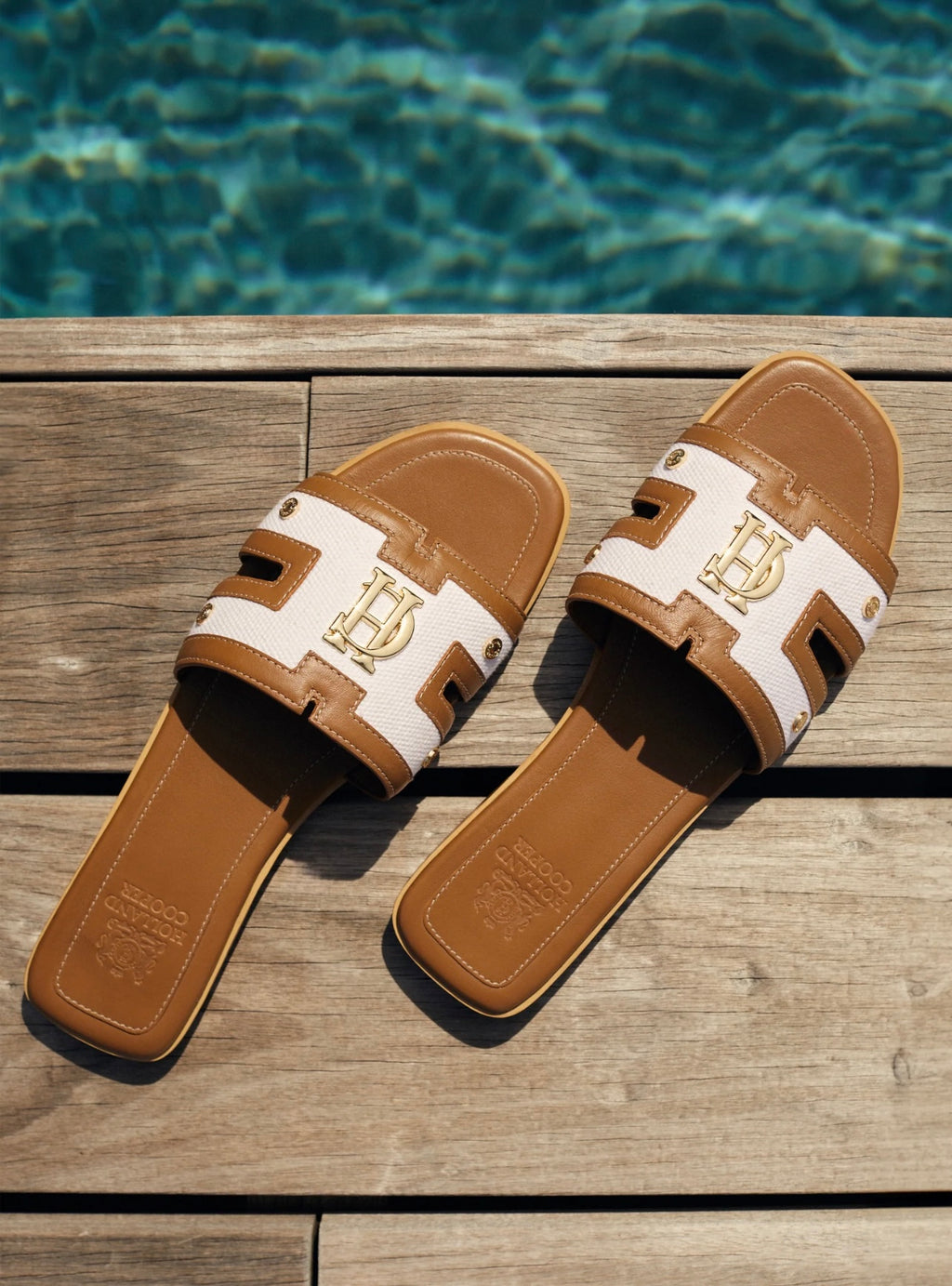 Brown and white sandals with a logo on a wooden surface with water in the background