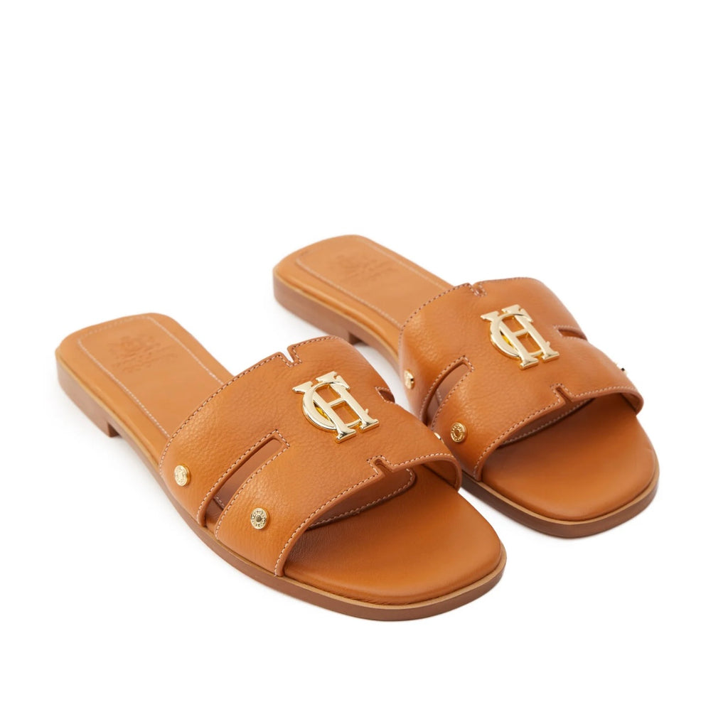 Pair of tan sandals with gold logo on a white background