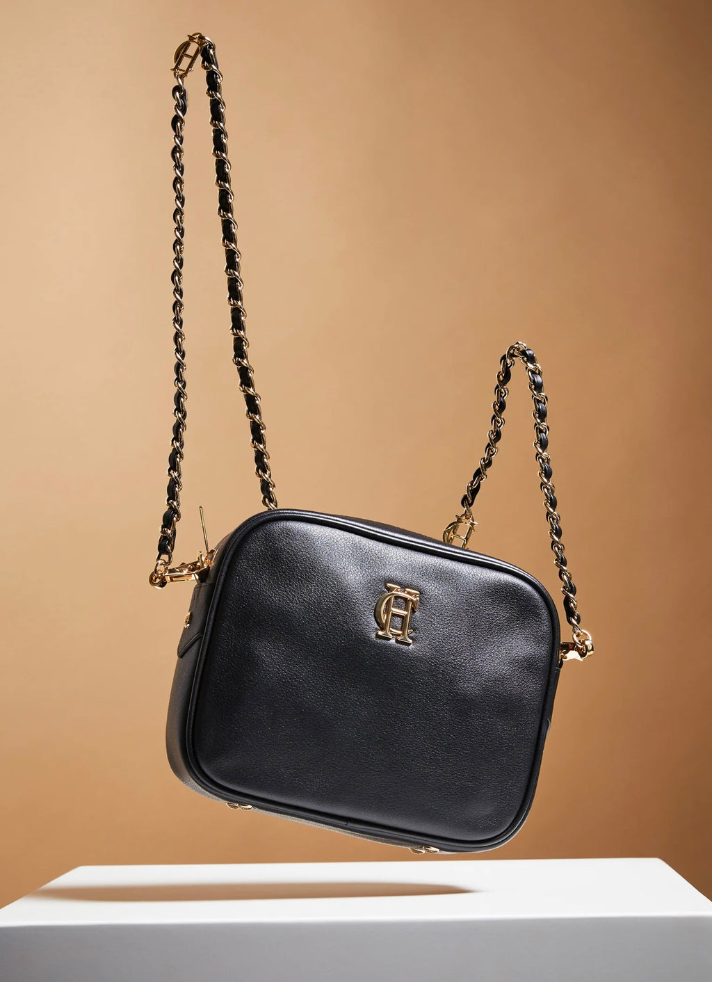 Black handbag with gold chain strap on a beige background