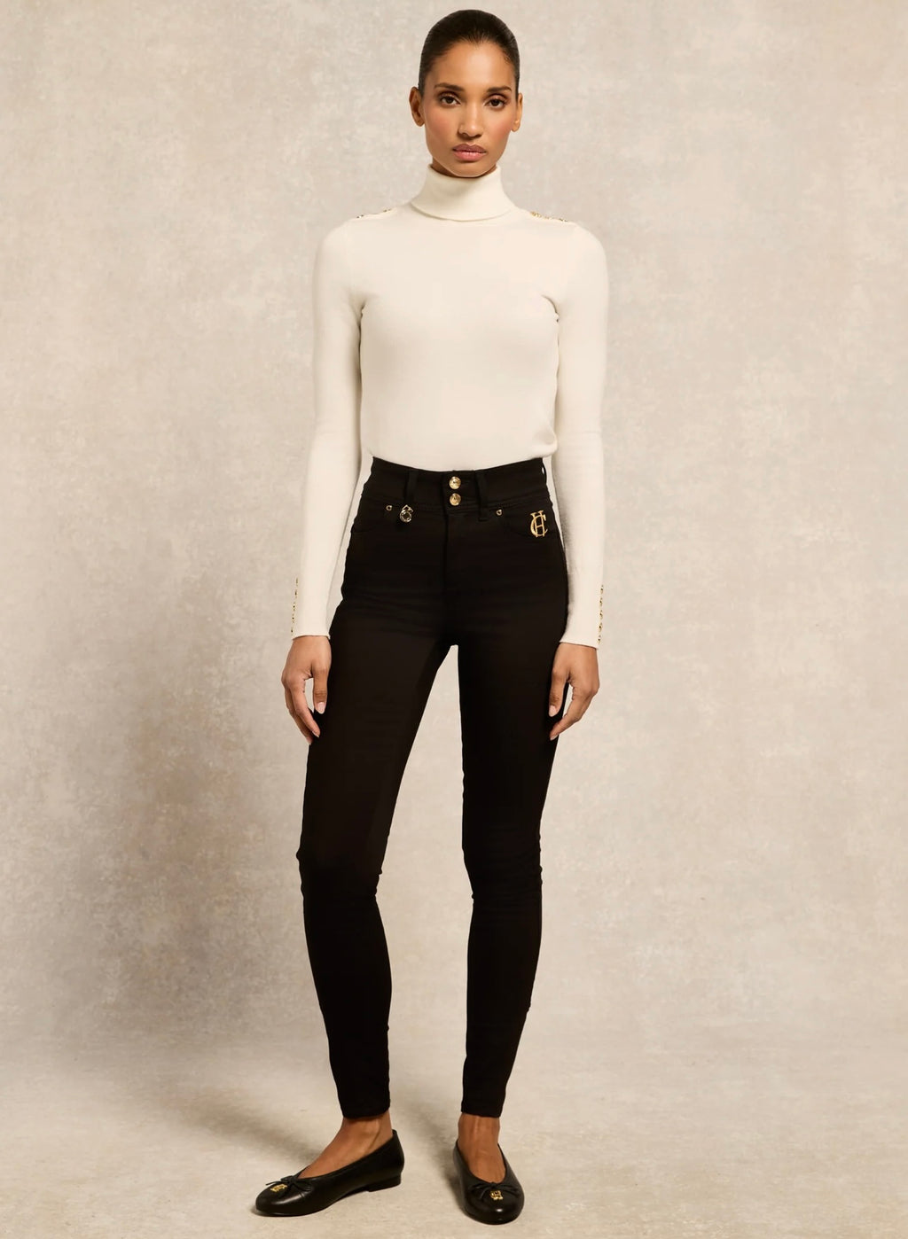 Person wearing a white turtleneck and black high-waisted jeans on a neutral background