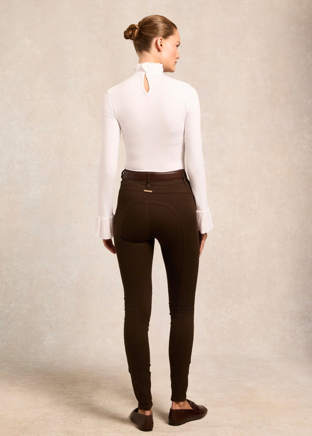 Person wearing a white shirt and brown riding pants on a plain background