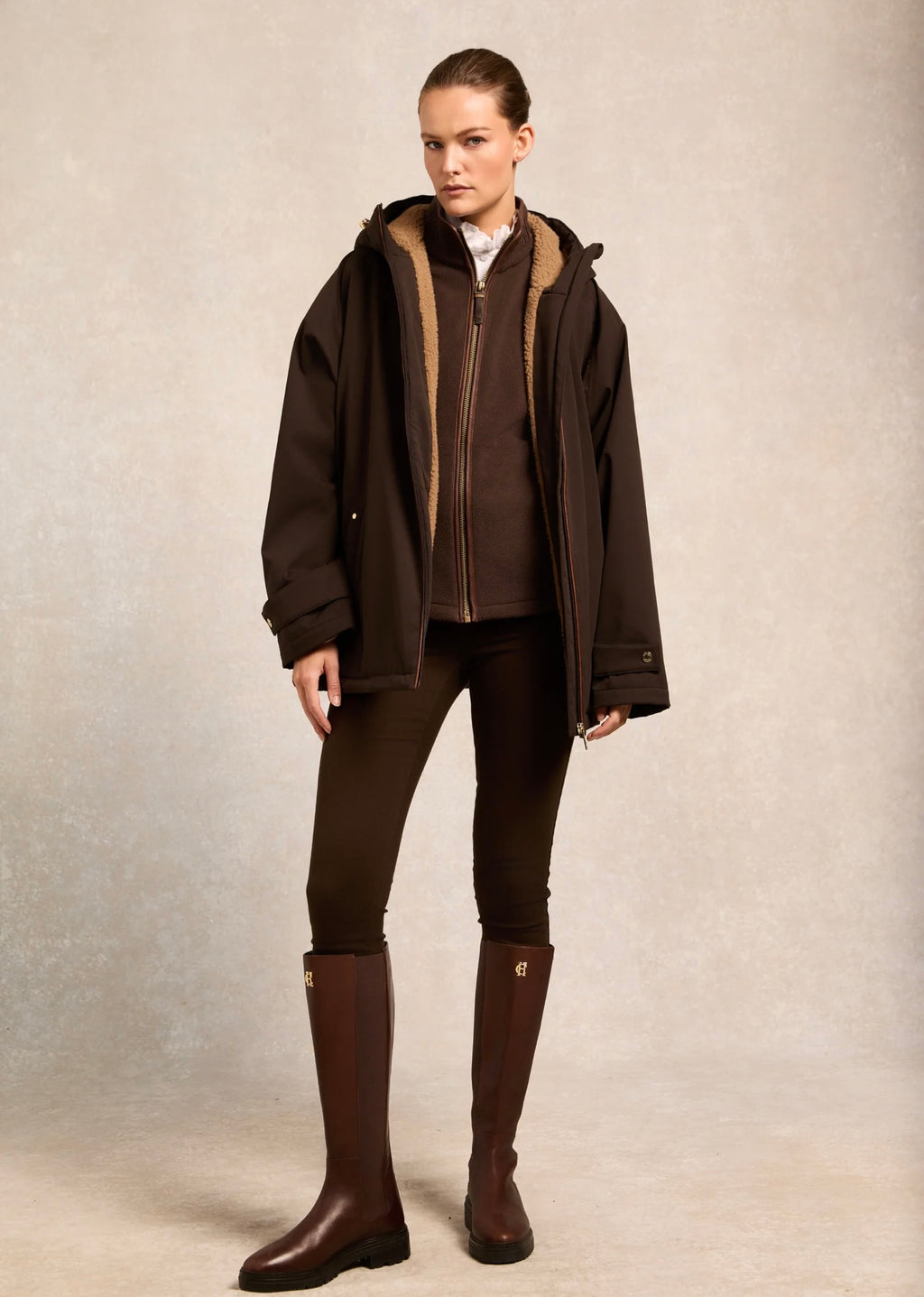 Woman wearing a brown jacket, leggings, and boots against a neutral background