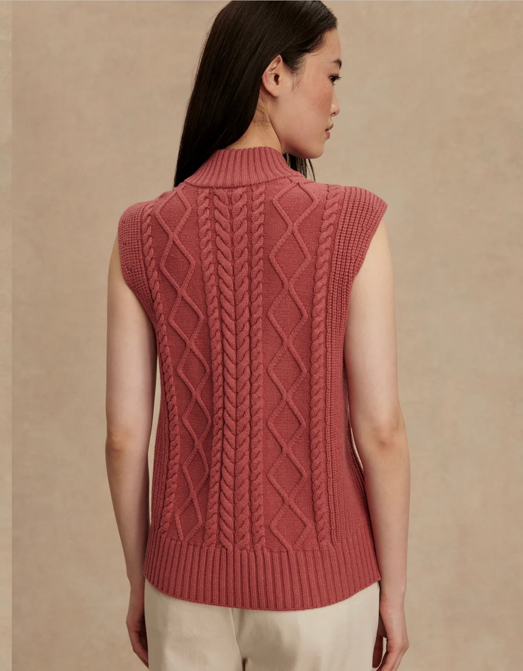 Woman wearing a pink knitted vest against a beige background