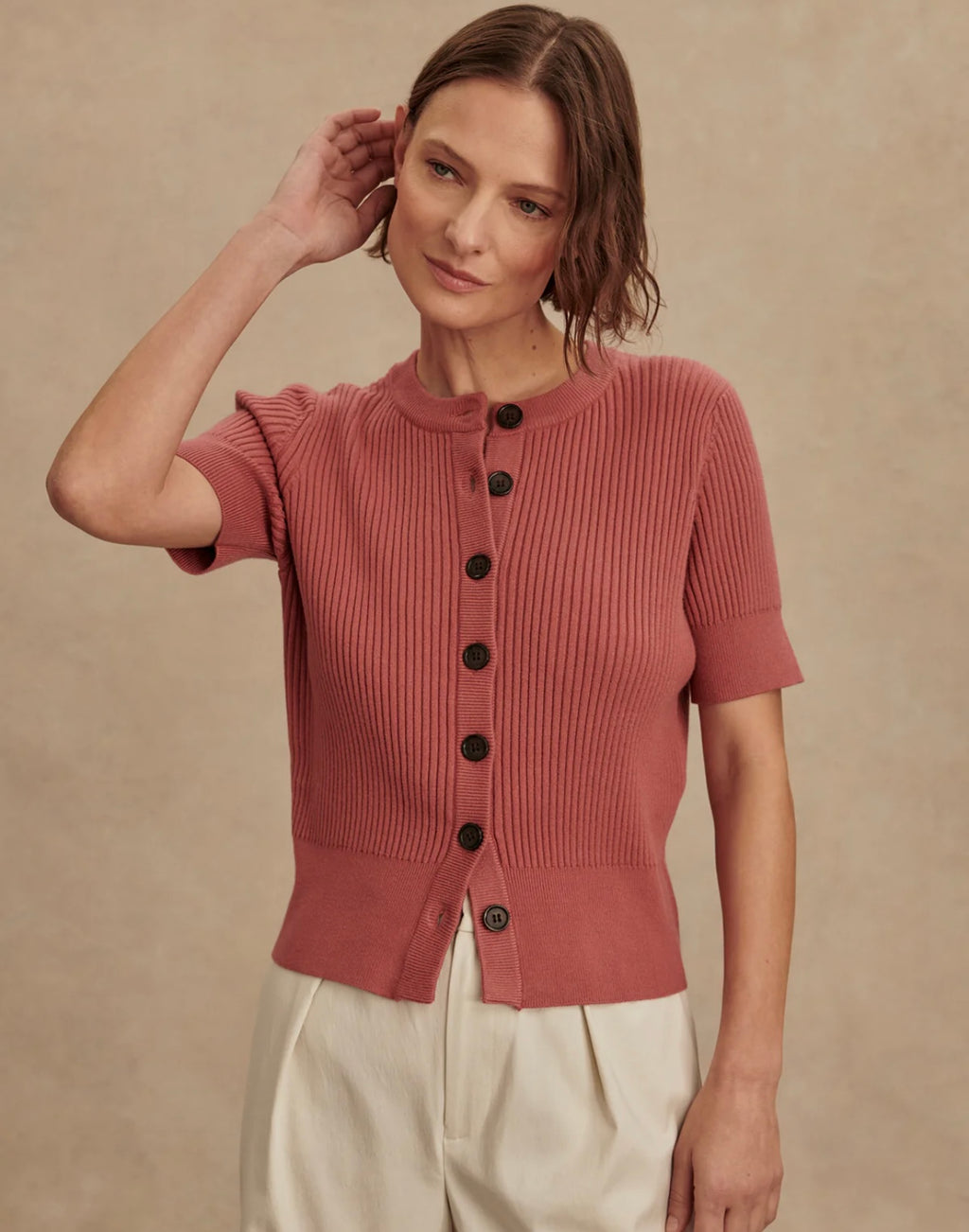 Woman wearing a pink ribbed sweater with black buttons against a beige background