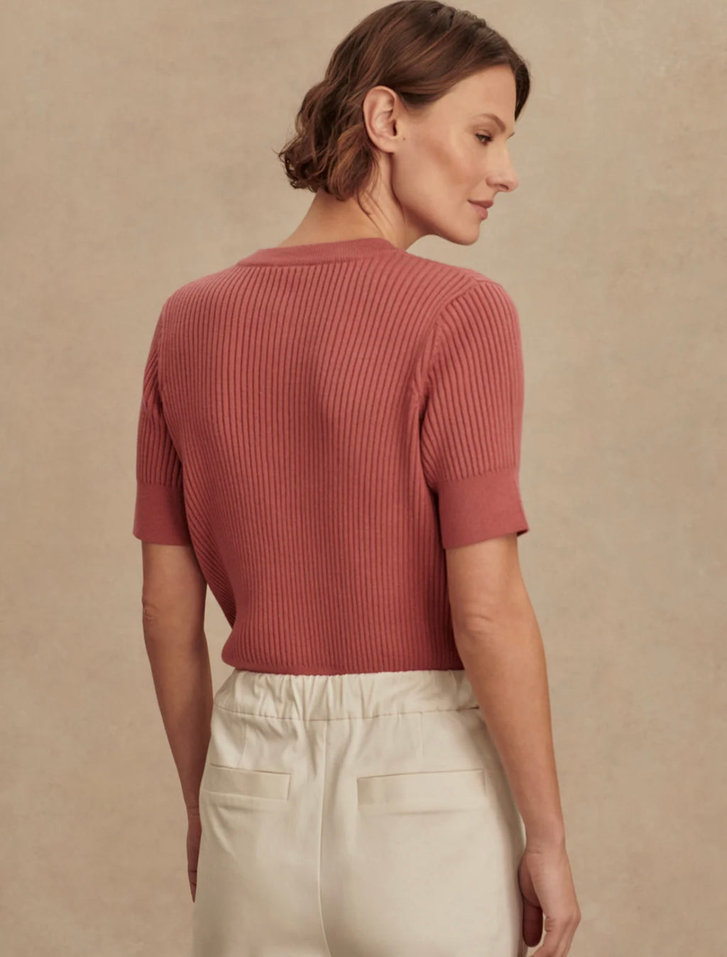 Woman wearing a pink ribbed sweater against a beige background