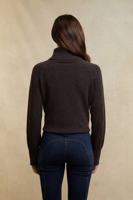 Person wearing a brown sweater and dark jeans against a beige background
