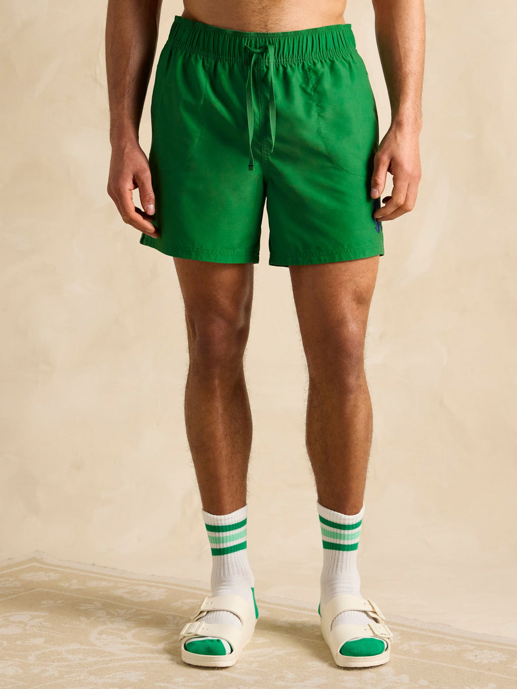 Person wearing green shorts and white socks with green stripes on a beige background