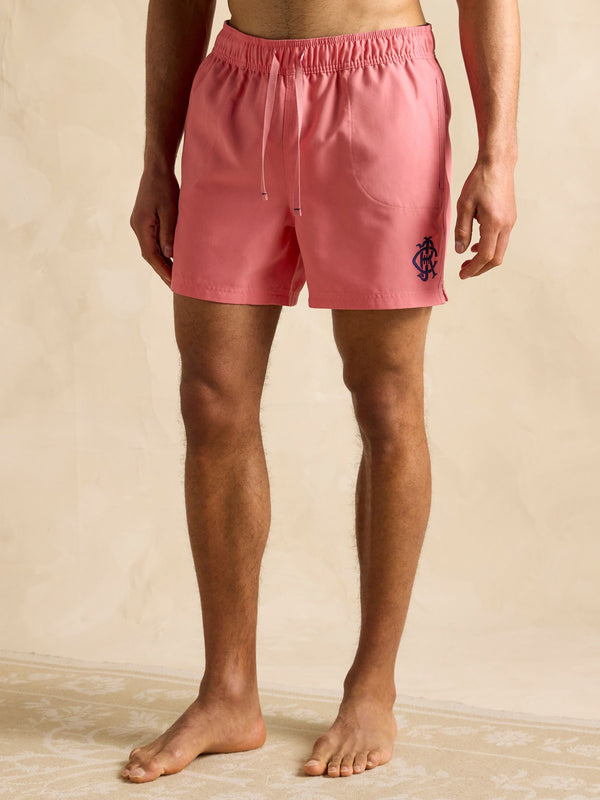 Person wearing pink shorts with a logo on a beige background