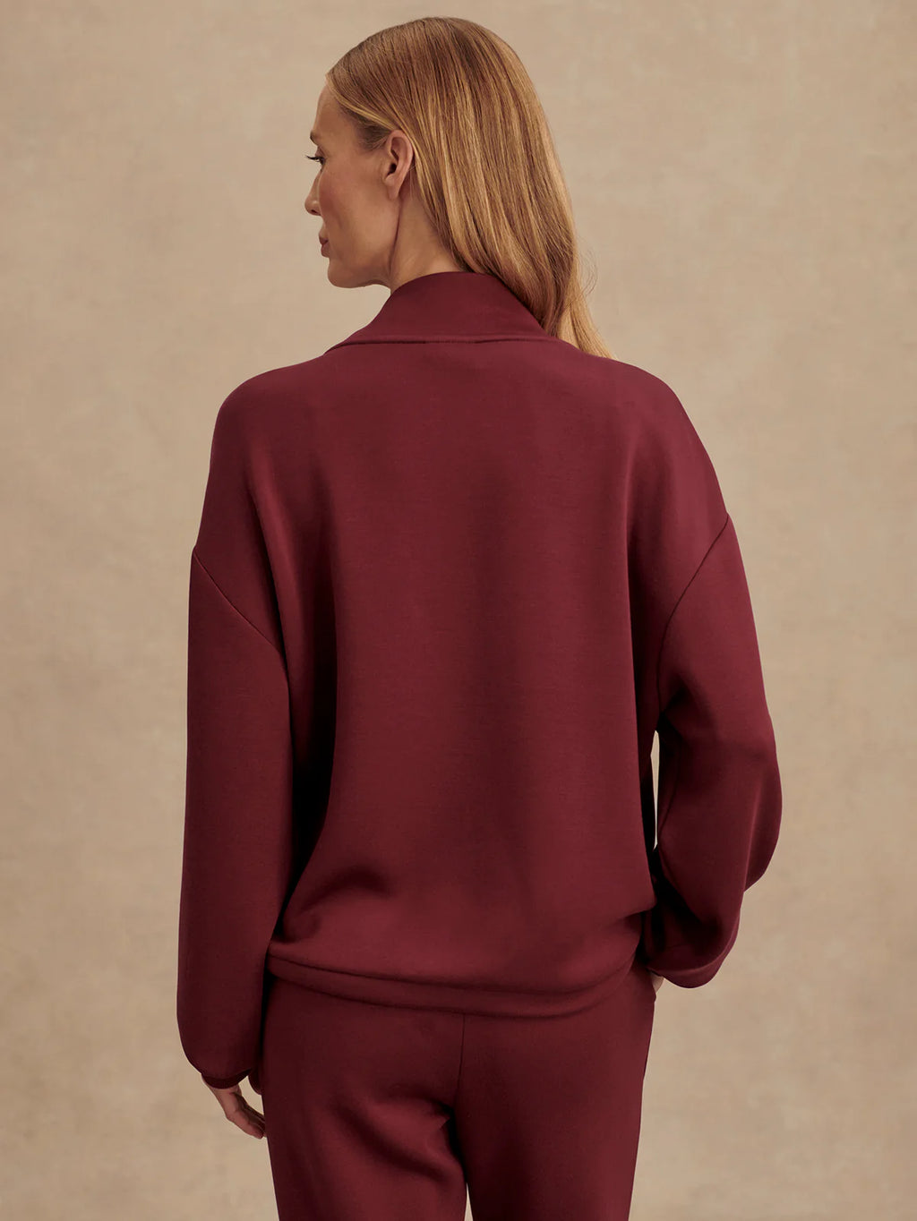 Person wearing a burgundy tracksuit against a beige background
