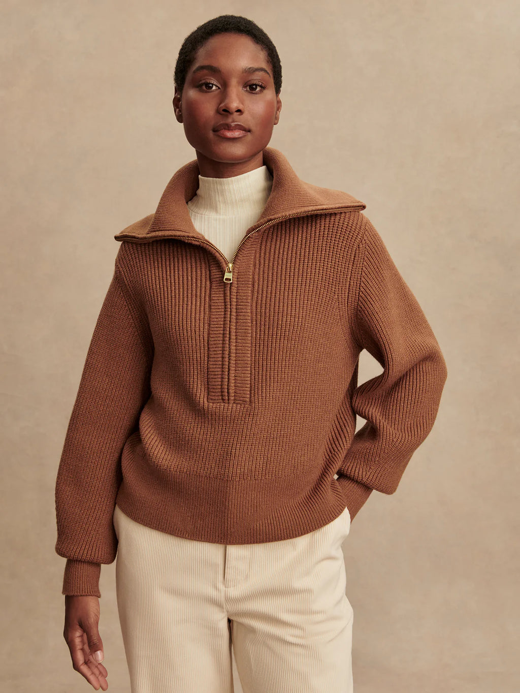 Person wearing a brown ribbed sweater with a high collar against a beige background