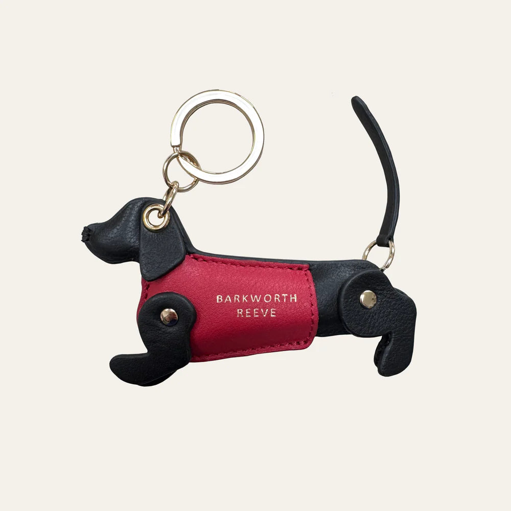 Dog-shaped keychain with red body and black legs on a beige background