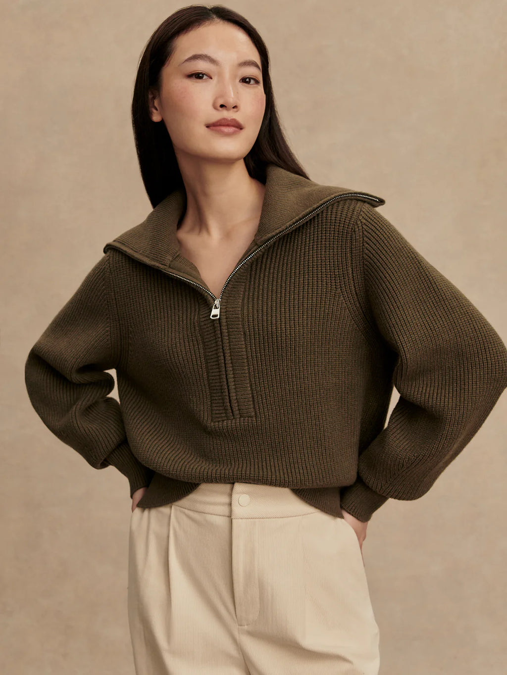 Woman wearing a brown zip-up sweater against a beige background