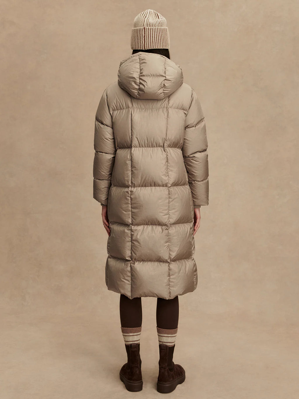 Person wearing a long beige puffer coat on a beige background