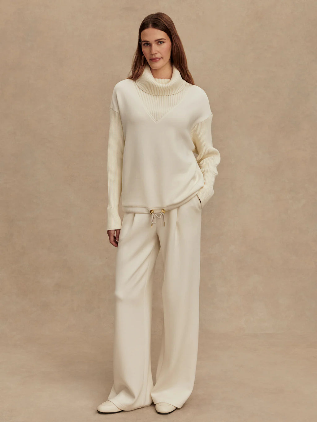 Woman wearing a white sweater and pants set against a beige background