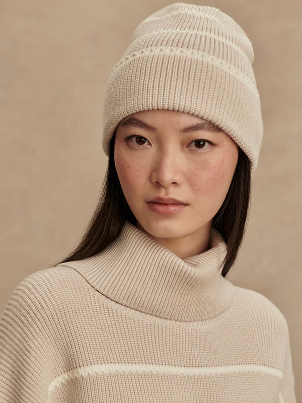 Woman wearing a beige knit hat and sweater against a beige background